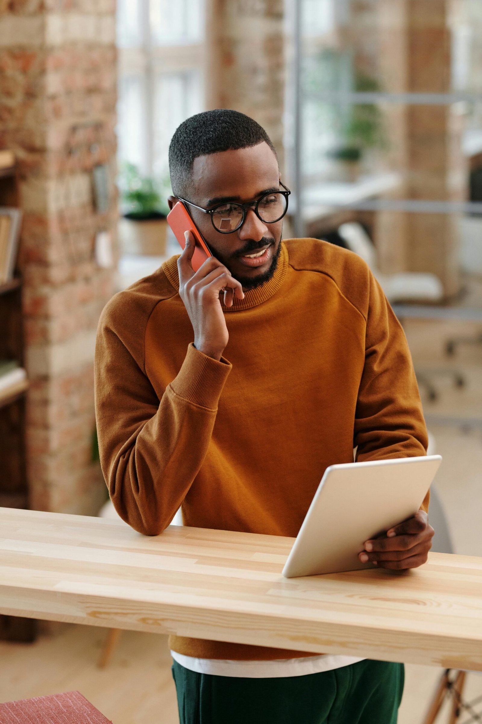 Young man in a modern office multitasking with a digital tablet and mobile phone.